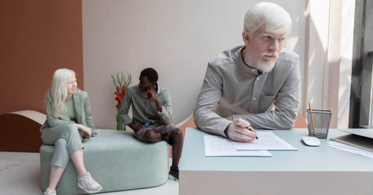 Different controls on document on the same route - Albino worker standing at table and writing on paper in office with African American man sitting with woman on background