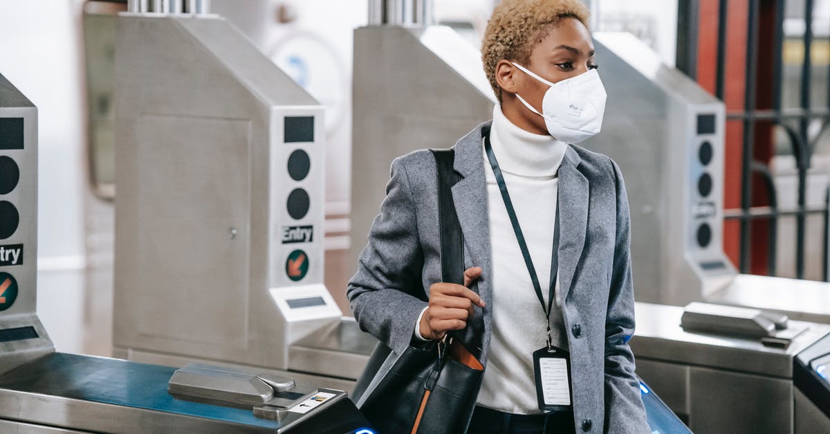 Difficulties with or reprimands for passing COVID hotspot? - Calm attractive African American female in stylish formal wear and protective mask passing through turnstile gates in underground station