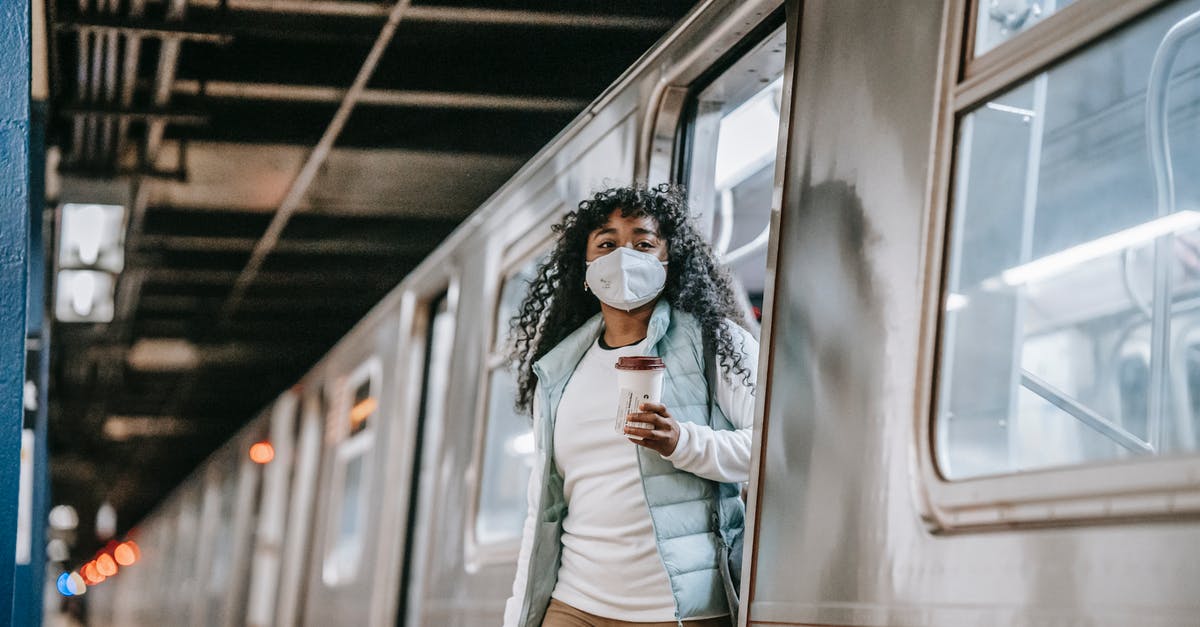Direct Airside Transit Visa (DATV) for South African [duplicate] - Young African American female passenger in casual clothes and mask drinking takeaway coffee and getting off train in subway station