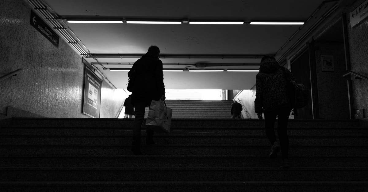 Direction to go to Australia -- where does it change? - Back view black and white of anonymous passengers walking up staircase leaving subway station