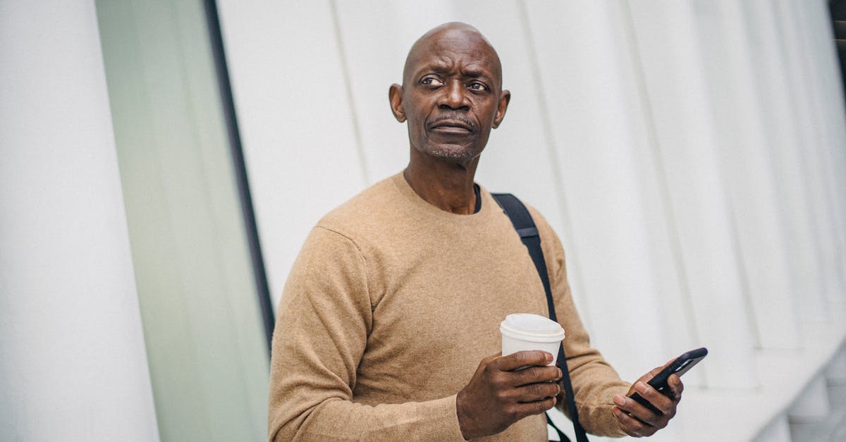 Direction to go to Australia -- where does it change? - Mature bald black man with smartphone and coffee cup standing on street looking around in downtown