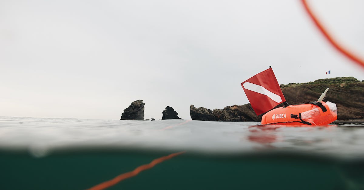 Diving safety in Australia - Red inflatable buoy with scuba flag floating in sea water near rocky formations