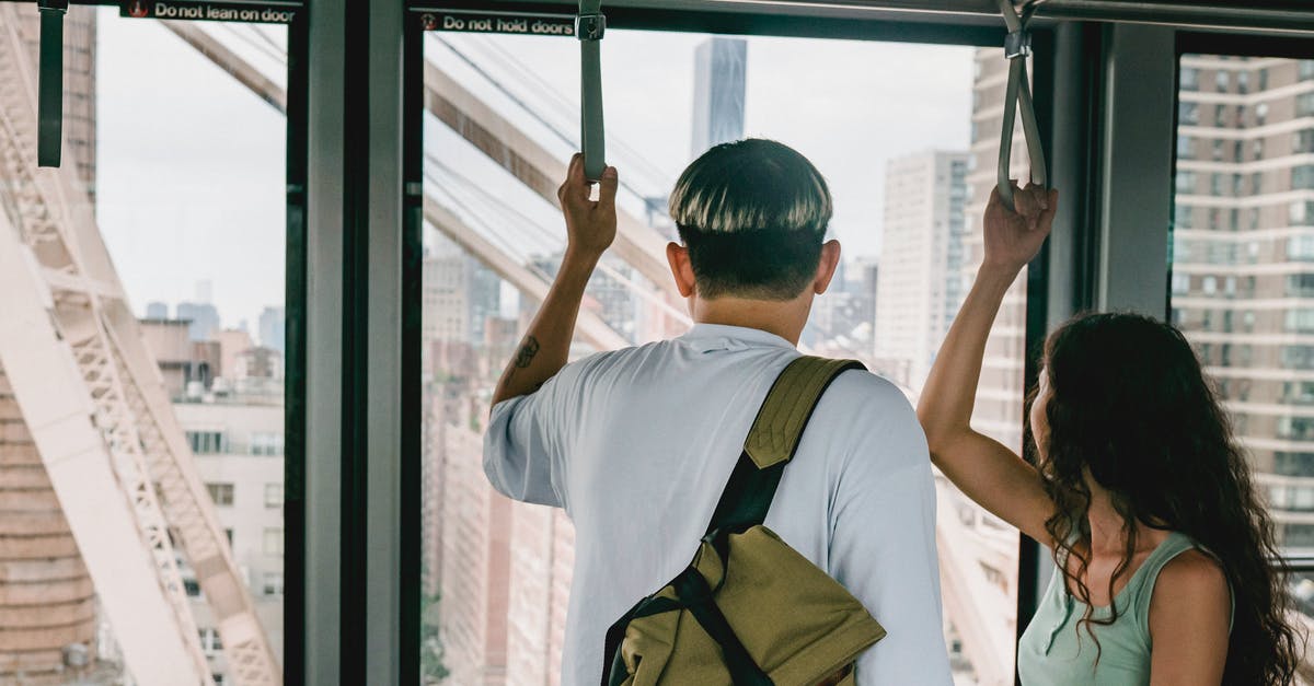 DIY London tour using public transport - Back view faceless couple in casual clothes riding funicular cabin and grabbing hangers while looking away on urban city views