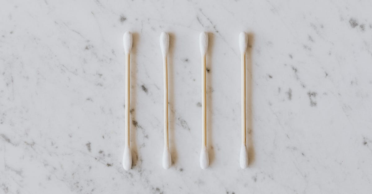 Do ear wax cleaning salons provide related, similar services? - Top view of identical cotton swabs on thin wooden sticks with soft rounded edges on marble surface with tiny spots and gray lines