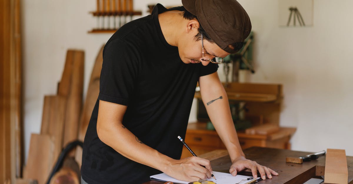 Do Etihad airways take dimensions of the check in baggage seriously? - Side view of Asian man in casual clothes and eyeglasses bending on table and taking notes by pencil while working in joinery