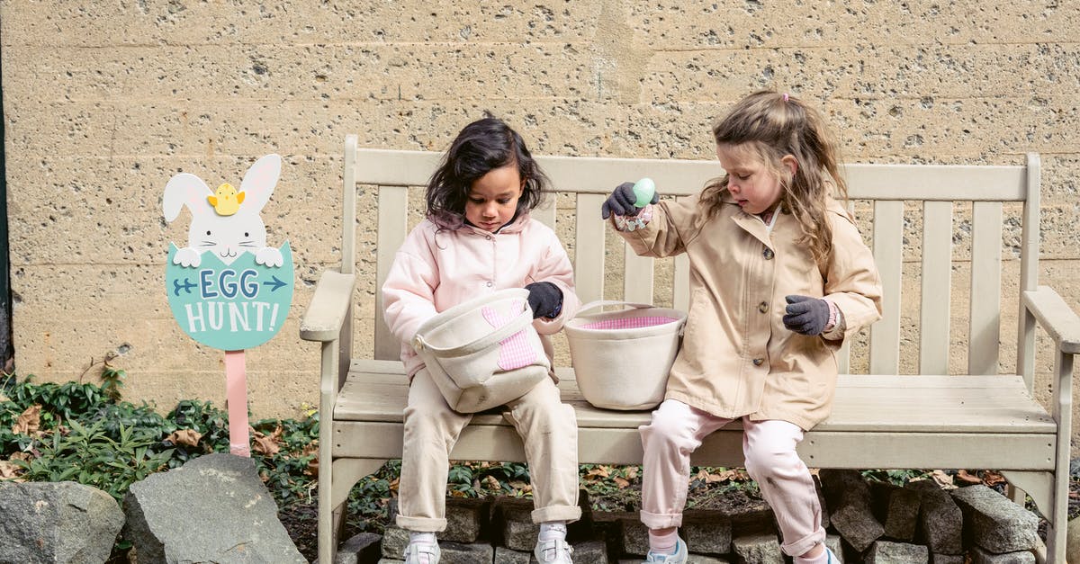 Do I have to collect my luggage when transiting through Moscow? - Full body positive cute diverse girls in warm clothes playing with Easter eggs and sitting on bench in backyard