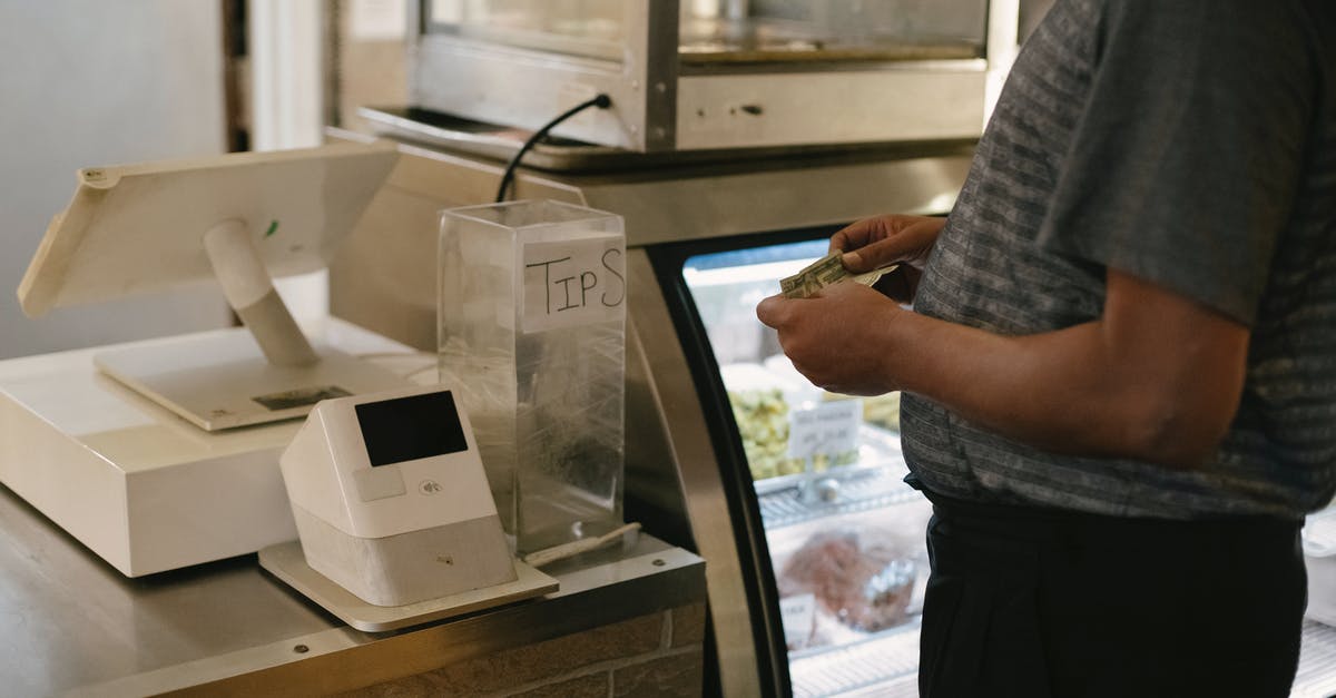 Do I have to pay double for checked baggage? - Unrecognizable male in casual clothes standing with money near cash register in grocery store while making purchase near glass showcase