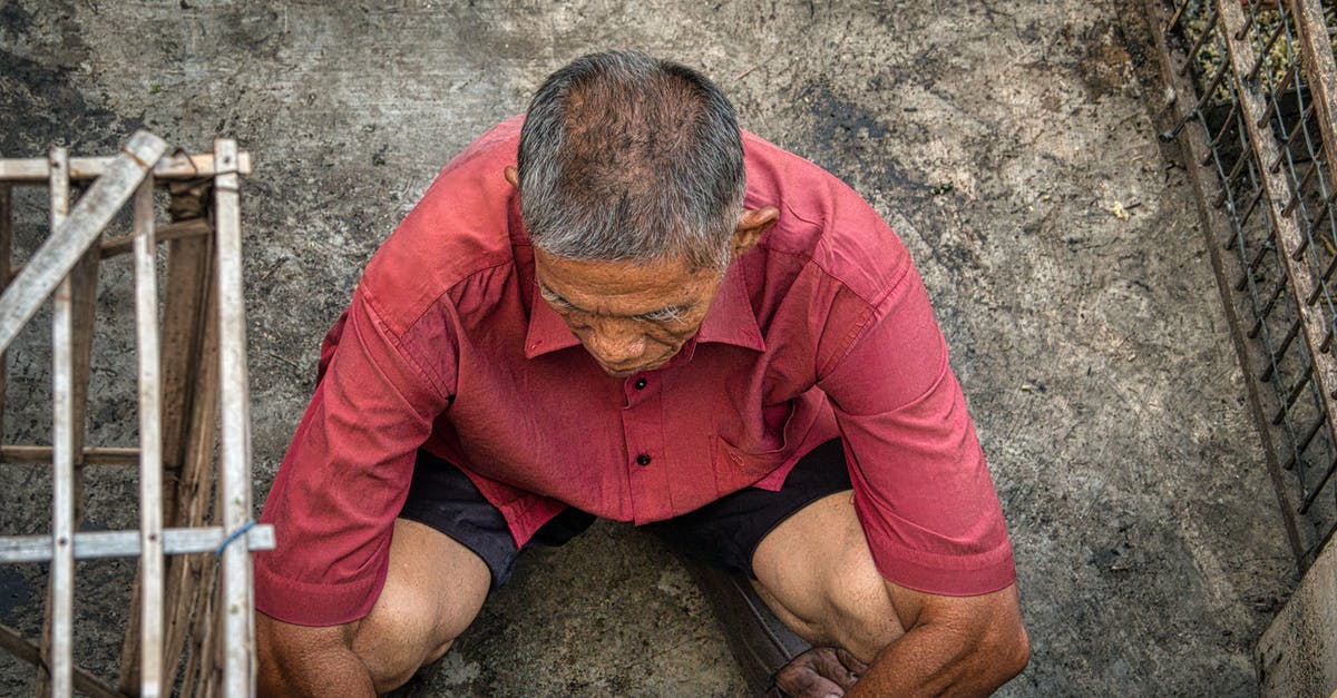 Do I need a Schengen visa from Jamaica? - From above of anonymous ethnic male squatting on dirty floor near grid on street in poor district of rural area