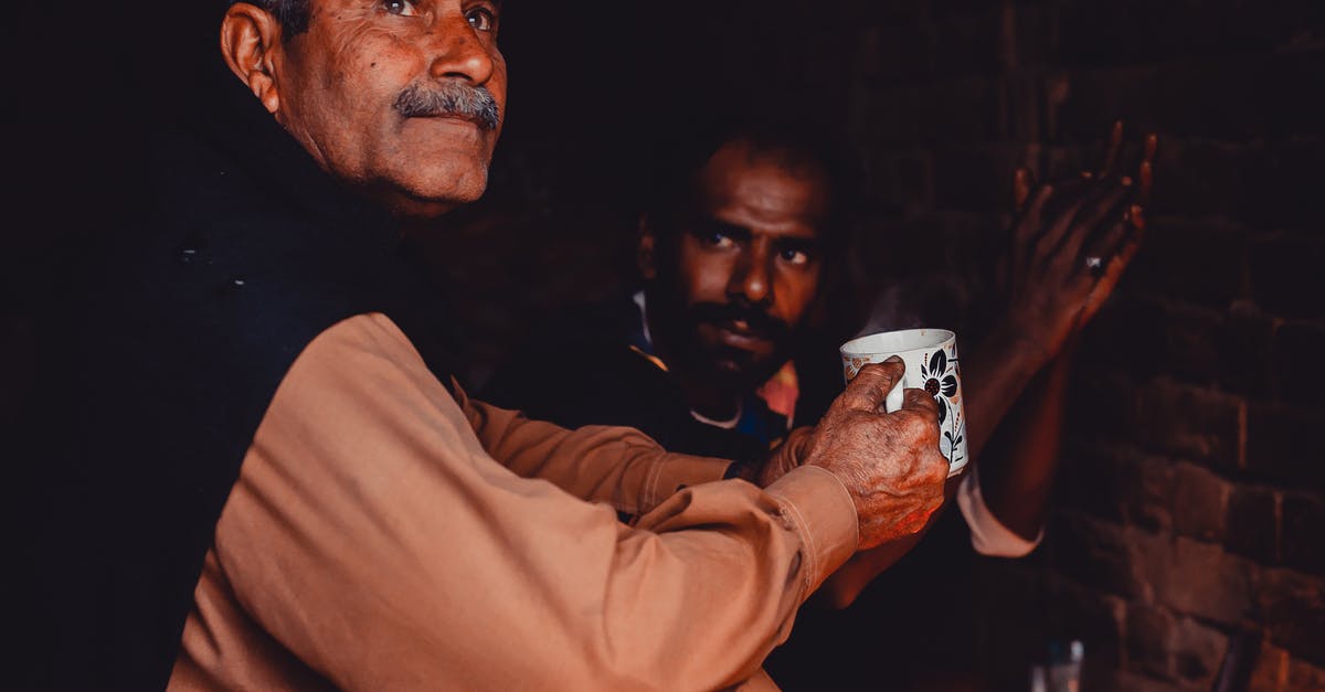 Do I need a transit visa with an Indian passport? - Old Indian man with gray hair and mustache sitting with cup of hot drink in brick poor building