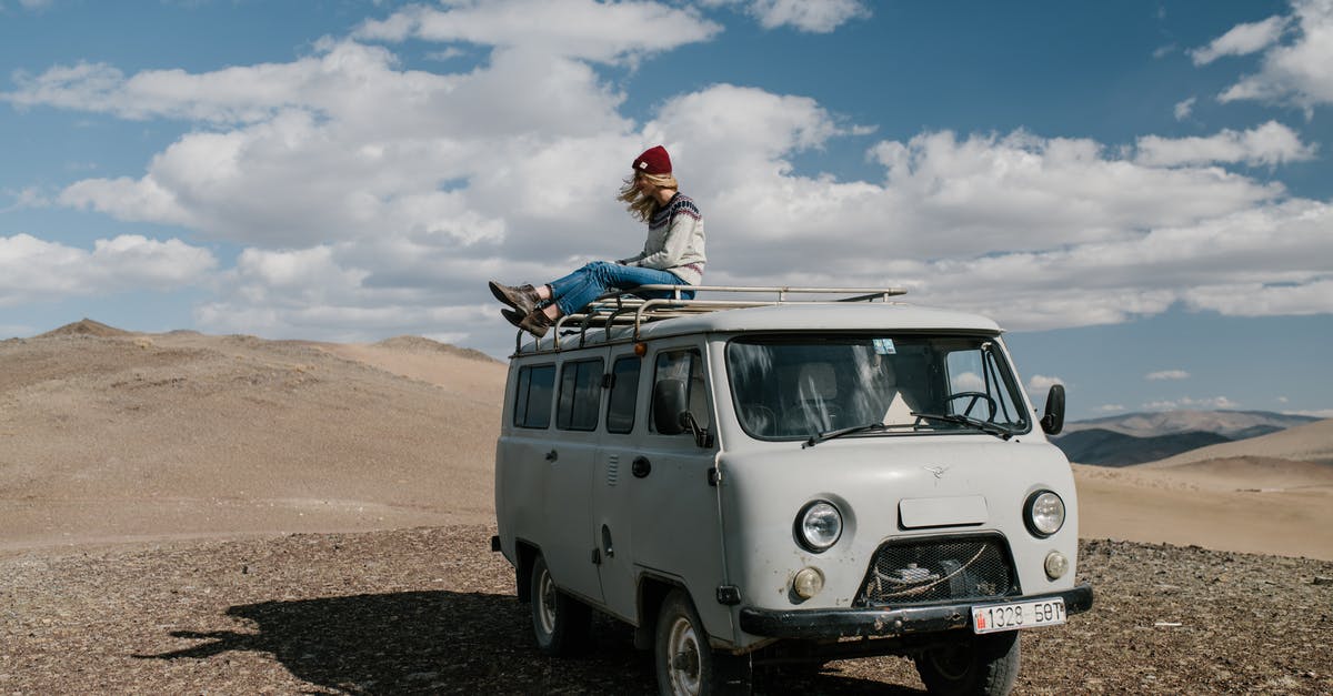 Do I need a vehicle rental to explore Miami FL? - Full length of anonymous female traveler sitting on roof of van in desert under cloudy sky