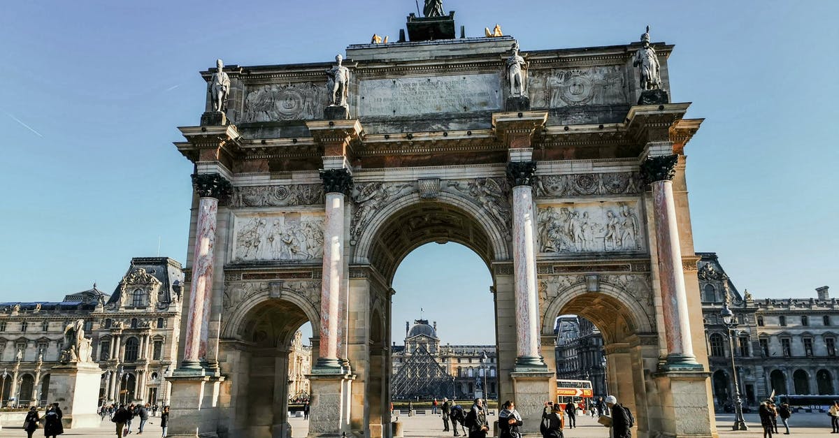 Do I need a visa to travel to Paris from London? - Old triumphal arch with sculptures on square with unrecognizable tourists