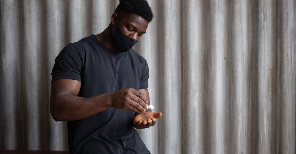 Do I need to apply for a new Schengen visa? - Black male athlete in sports clothes and textile mask applying antiseptic gel on hand against ribbed gray wall