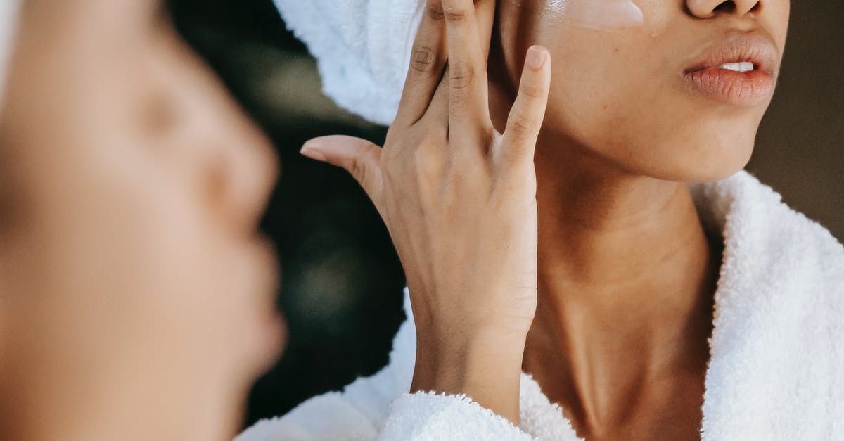 Do I need to apply for ESTA? - Crop unrecognizable young ethnic female in terry robe applying moisturizing cream on cheek while reflecting in mirror