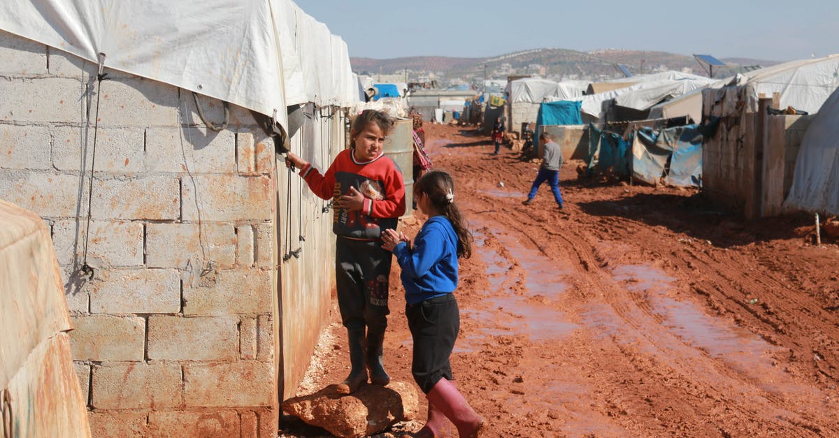 Do I need to pass through immigration in CDG? - Full body of preschool and teenage ethnic girls speaking near weathered old brick residential building in poor settlement