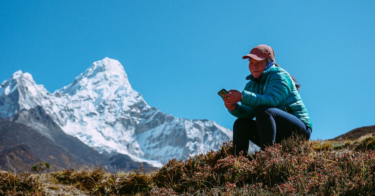 Do I need to pick up luggage for transit? - Tourist Girl Sitting on Mountain Meadow with Phone in Hand