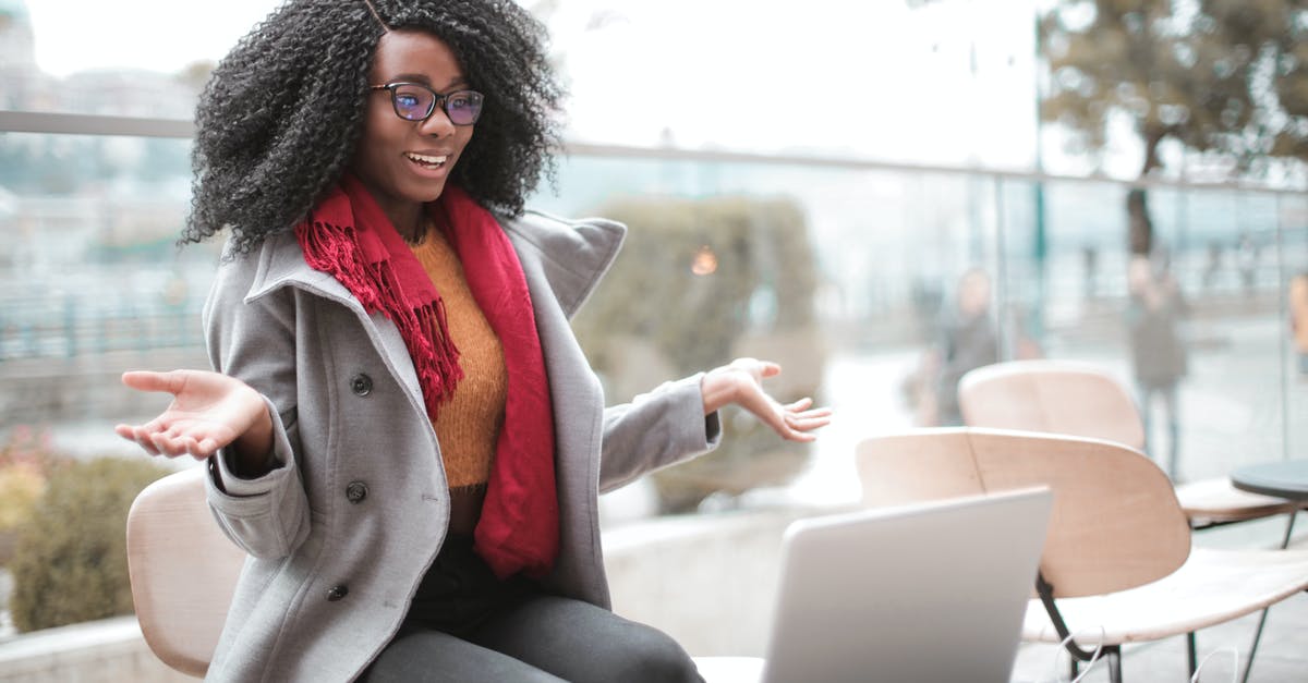 Do many Japanese people speak Korean? - Happy excited African American female laughing and gesticulating while having video calling on laptop and sitting at modern cafe