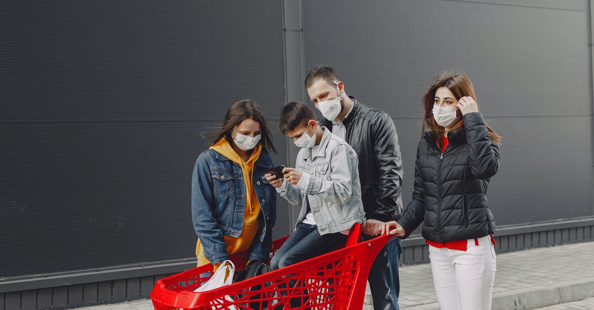 Do Medical Devices Count as Carry-On or Personal Item? - Happy family in casual clothes and medical masks standing on street after shopping while kid sitting in trolley and playing games on smartphone