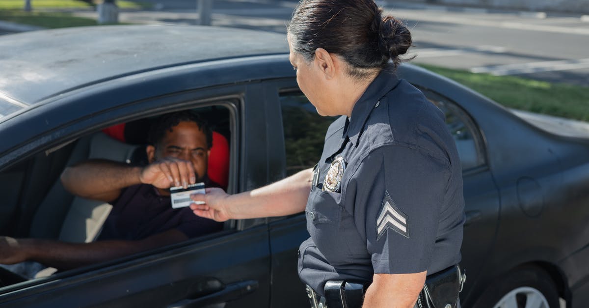 Do North-American car rental agencies typically apply a minimum driving license duration? - Man Giving His Driver's License to the Policewoman 