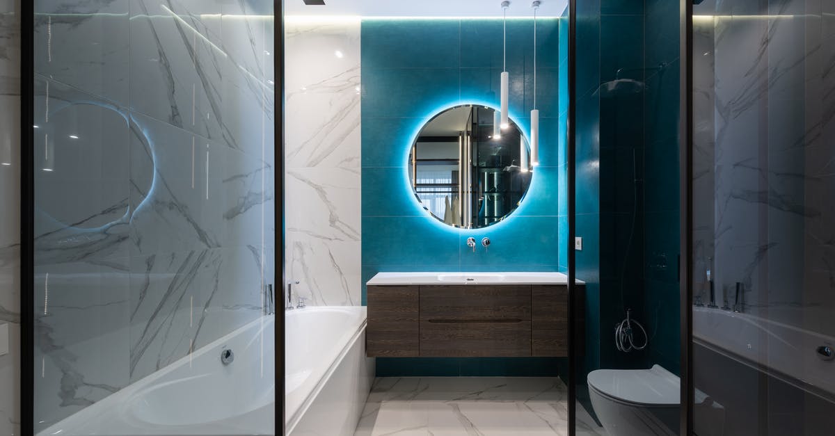 Do the new Canadian hotel quarantine requirements apply to non-residents? - Round mirror with neon illumination hanging over sink in modern bathroom with white ceramic toilet bowl and bathtub