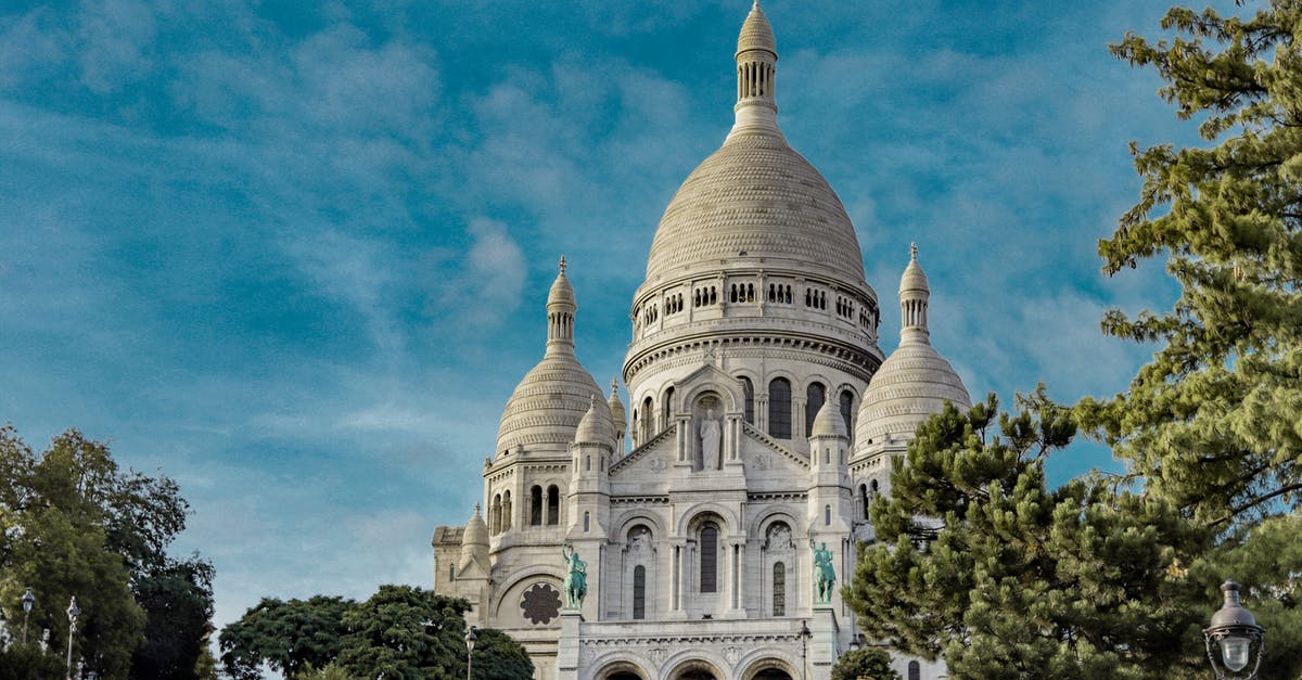 Do we need a visa for an overnight trip UK to Paris and back? - Low angle exterior of famous Sacre Coeur Basilica with domes and arched windows located on Montmartre hill in Paris against blue sky