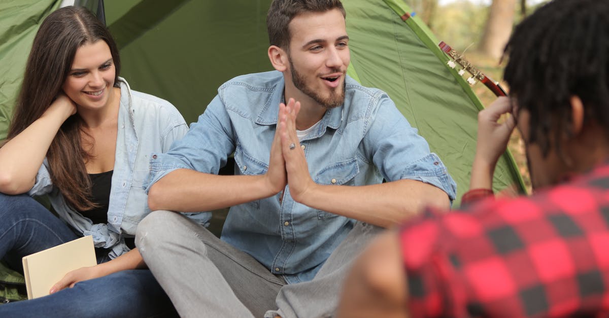 Do you have to book motels in advance on a road-trip? - Group of friends having fun in camp while man sitting in lotus position with namaste gesture and talking