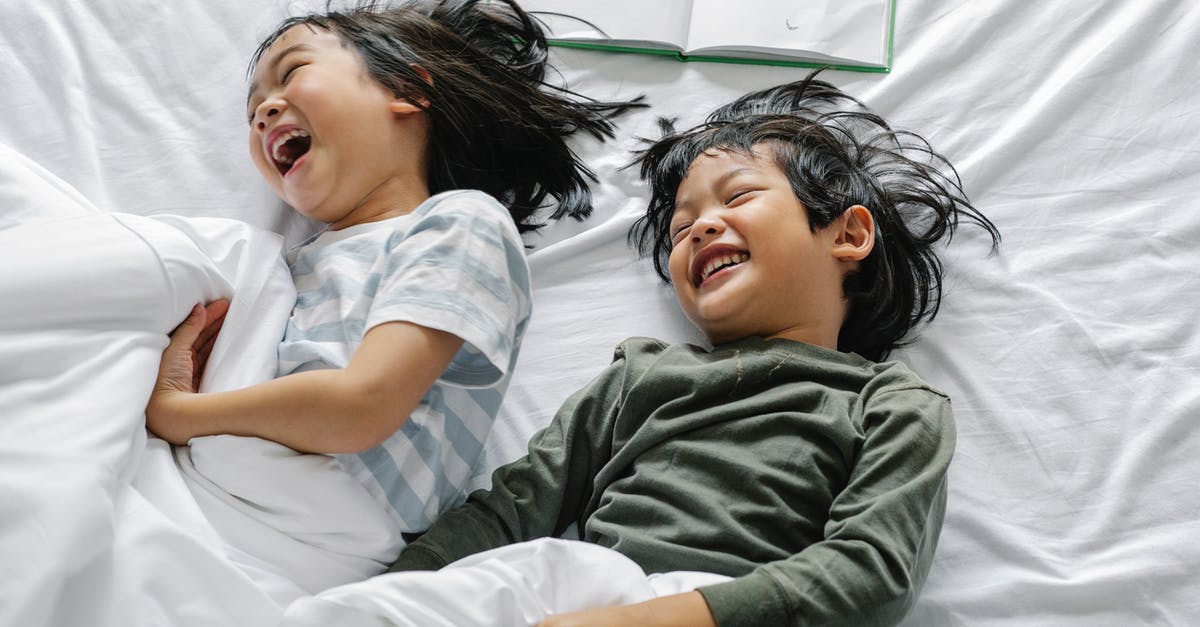 Do you have to book motels in advance on a road-trip? - From above of Asian boy and girl laughing and smiling while lying in sleepwear on bed in morning n bedroom