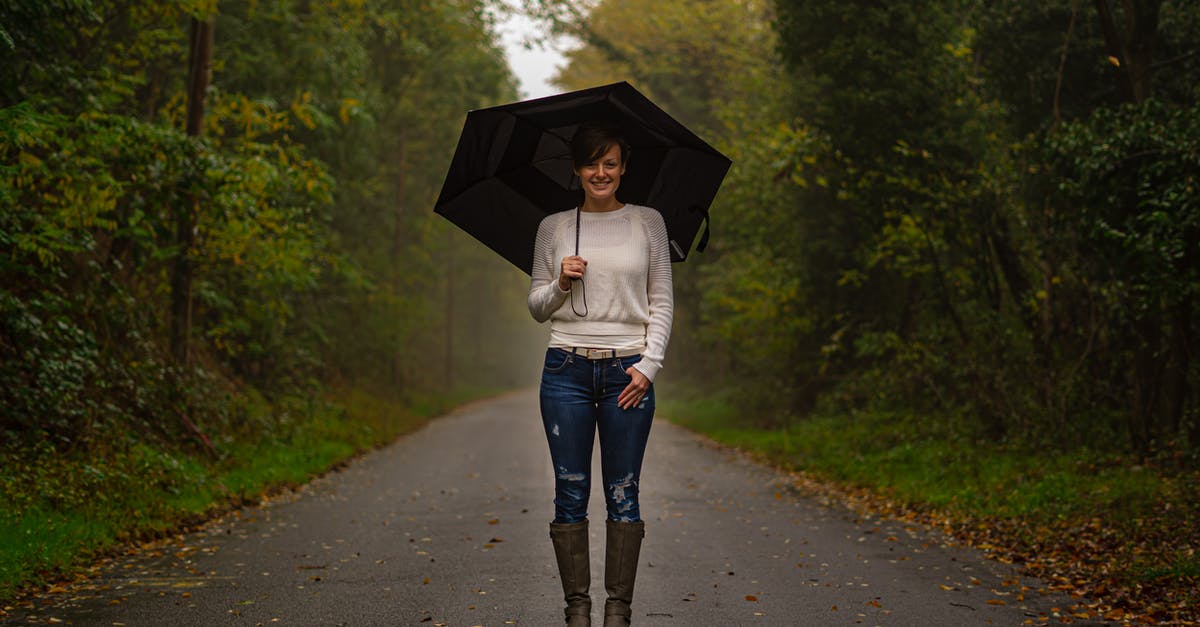 Do you need rain boots for June in Paris? - Woman in White Top and Blue Denim Jeans Holding Umbrella Walking on Road