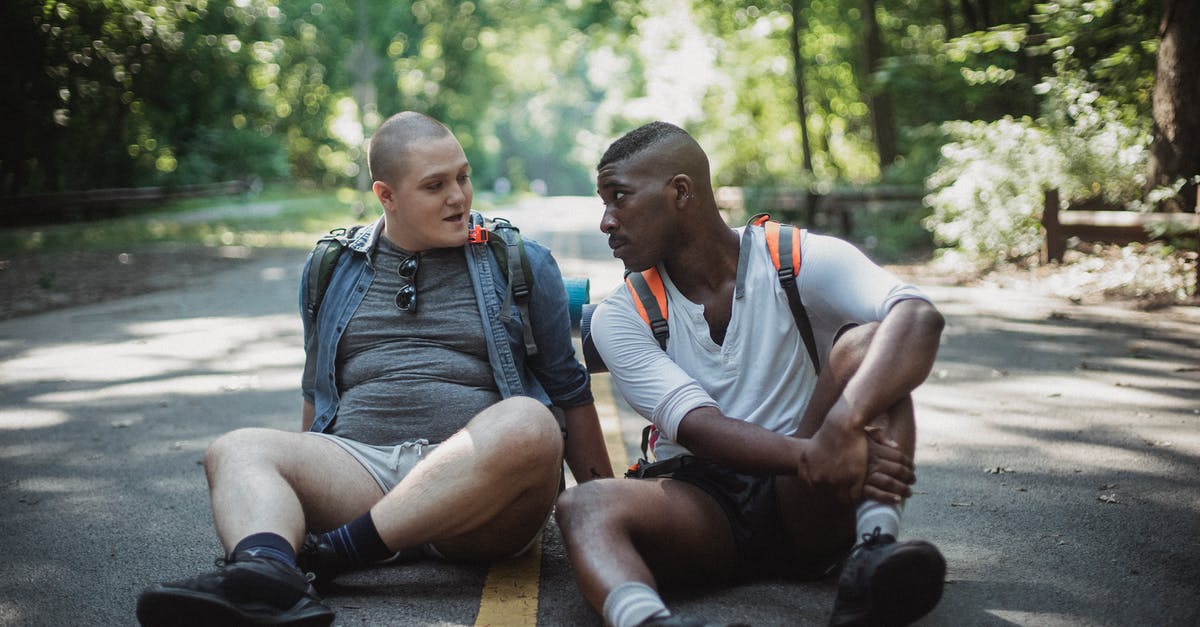 Does a UK entry ban affect travel to other countries? [closed] - Calm diverse homosexual couple with travel backpacks sitting on asphalt roadway and looking at each other in sunny day