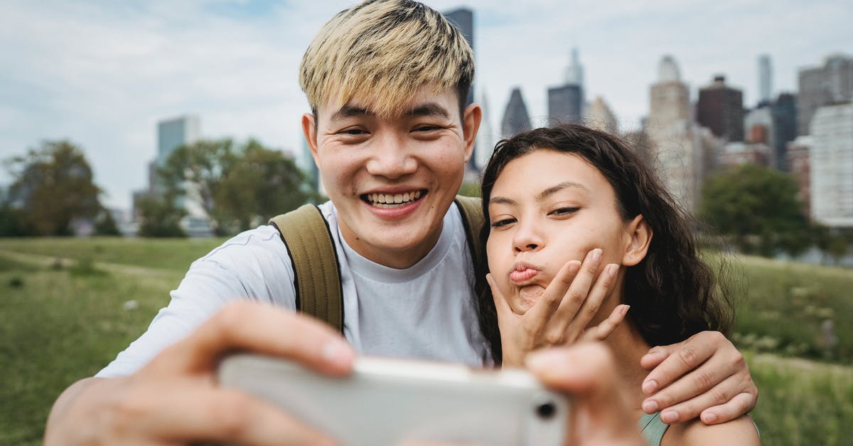 Does Google Maps have ferry schedules and make use of them? - Cheerful Asian boyfriend hugging ethnic girlfriend making grimace while taking self portrait on cellphone in green city park