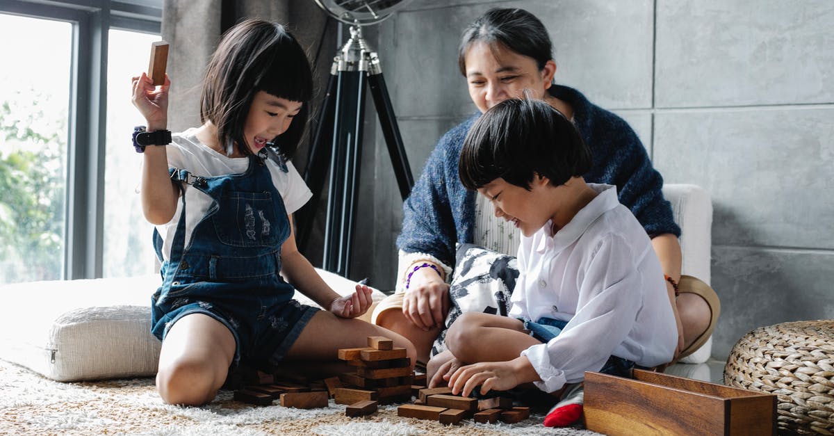 Does Indigo have manual check-in to get boarding pass? - Cheerful little Asian siblings sitting on carpet with grandmother and playing tower game during weekend at home