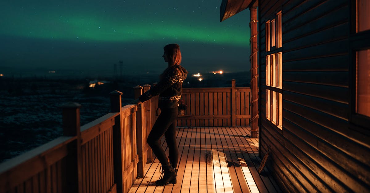 Does night-driving-friendly, polarized eye-wear exist? - Side view of anonymous female in casual wear standing on wooden balcony of house and looking at majestic polar lights in dark sky