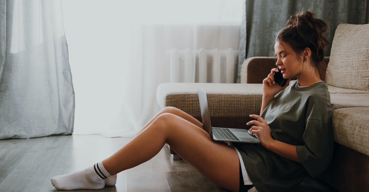 Domestic to International connection at LAX - Side view of young female in domestic outfit sitting on floor near sofa and browsing netbook while talking on mobile phone at home