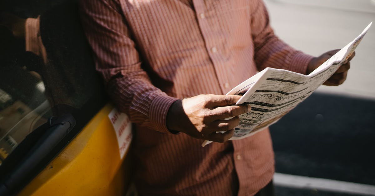 Don't have news about my eTA process, what should I do? - Crop anonymous ethnic cab driver in ornamental shirt standing with newspaper near transport in sunlight