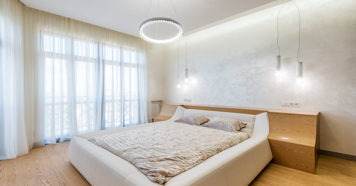 Double bed in Germany - Interior design of minimalistic modern bedroom furnished with comfortable bed and bedside nightstands decorated with ring shaped chandelier and lamps on ceiling