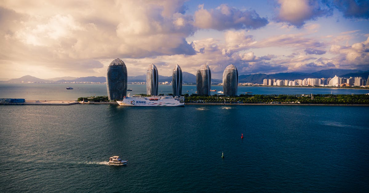 Double entry visa to China when visiting on a cruise ship - Modern cruise ships and boats floating on calm sea against cloudy sky near futuristic skyscrapers located on Phoenix Island in China