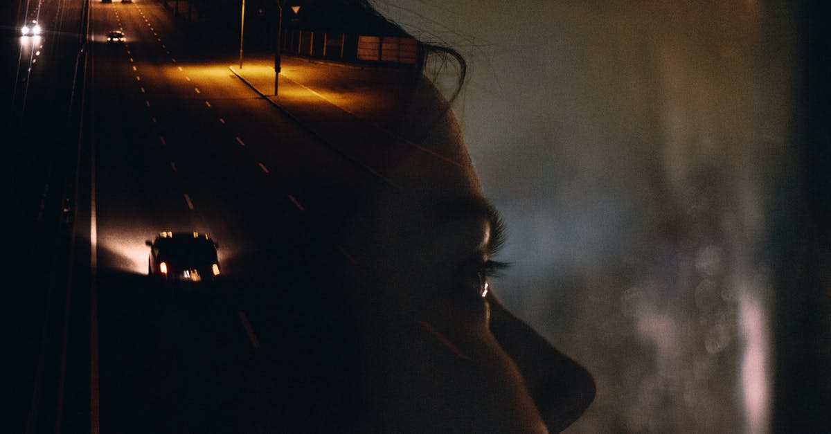 Driving a rental car through Colorado - Side view crop female sitting in car behind window glass reflecting road with moving cars and street lights at night