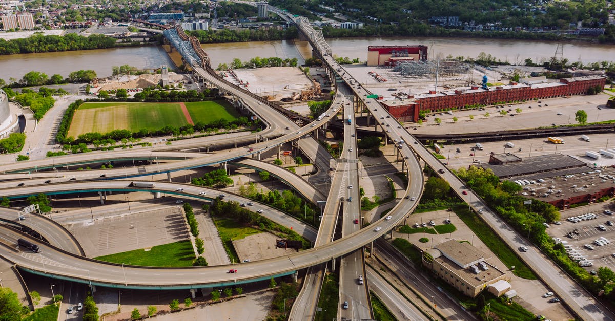 Driving distance between O'Hare (ORD) and Downtown Chicago is 20.5 mi and 1H 17min? - Drone view of modern cars riding through junction above greenery and broad river