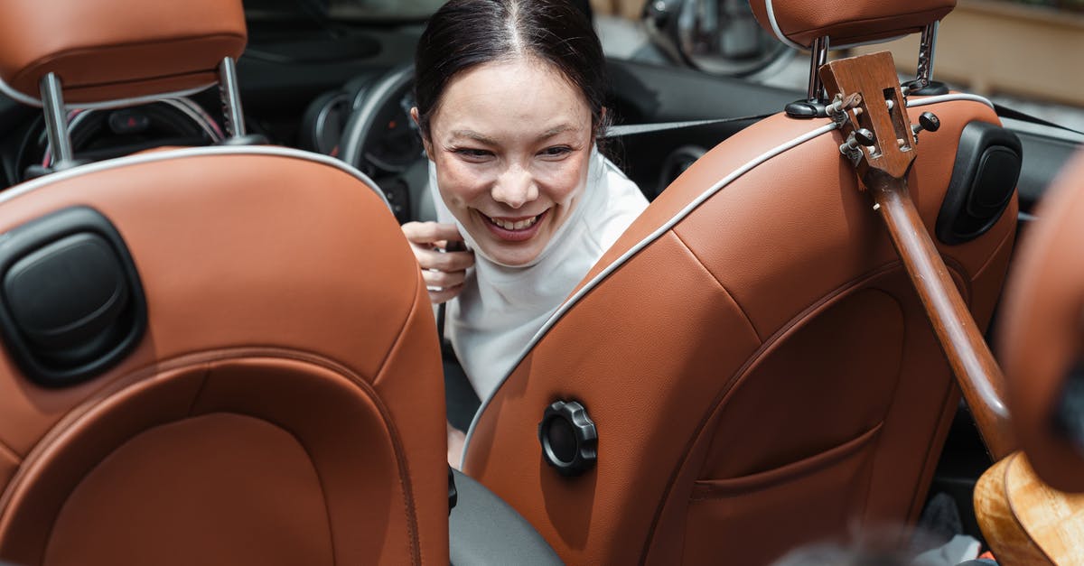 Driving from Berlin to Auschwitz-Birkenau - From above of smiling ethnic female driver turning back and looking at unrecognizable kid with ukulele during road trip