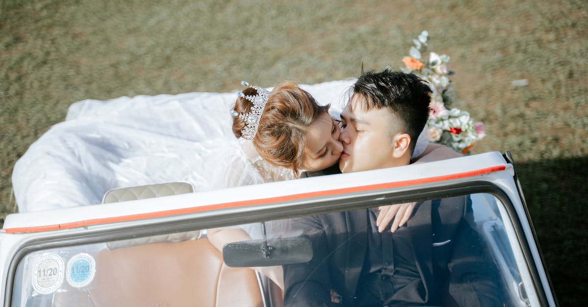 Driving from Denver to DC in December [closed] - From above Asian bride in wedding dress and groom in elegant suit sitting on driver seat in retro car kissing each other