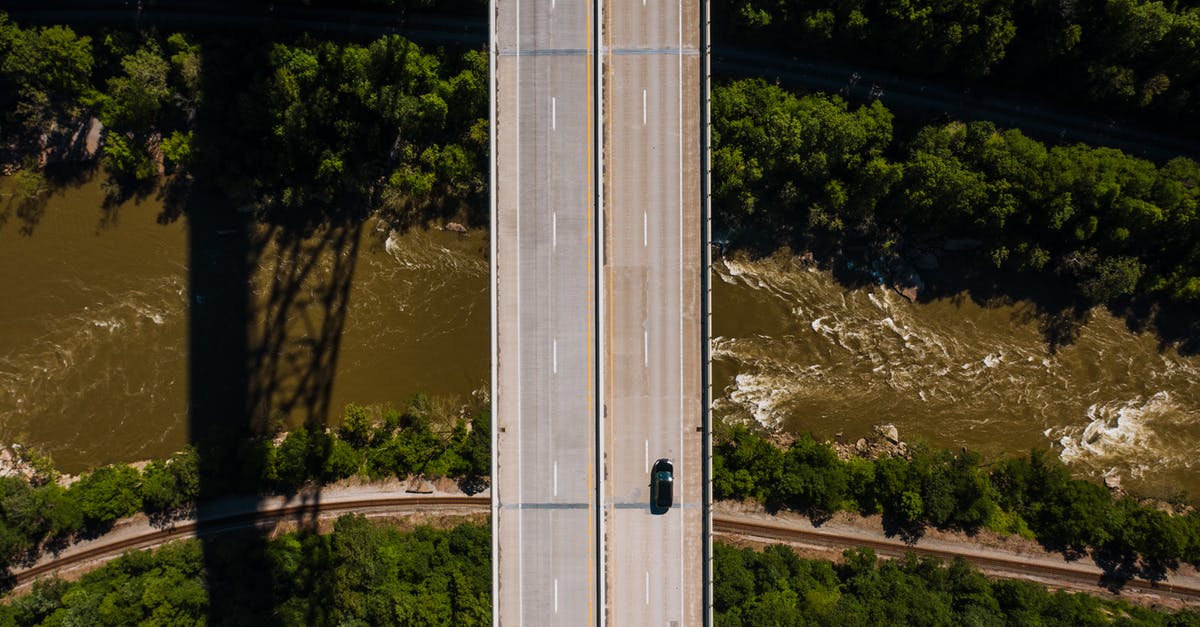 Driving from Seattle to Campbell River, BC - Aerial view of lonely car driving along asphalt bridge road crossing wild river running through green forest