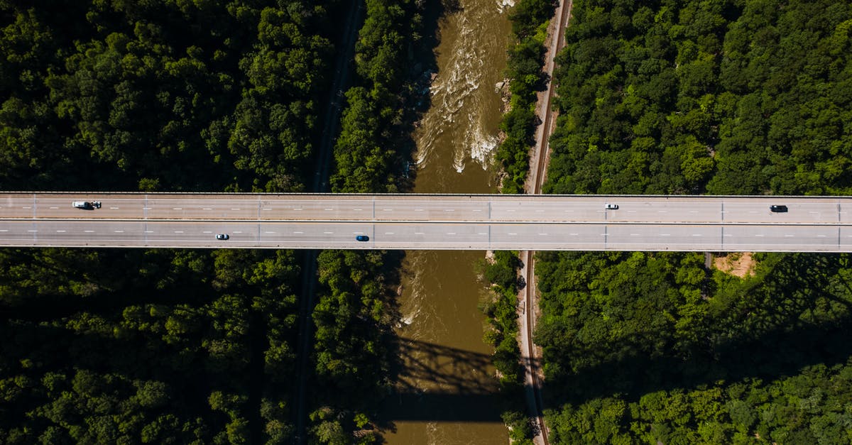 Driving from Seattle to Campbell River, BC - Breathtaking drone view of modern bridge road with driving cars crossing brown river flowing between lush green woods on sunny day