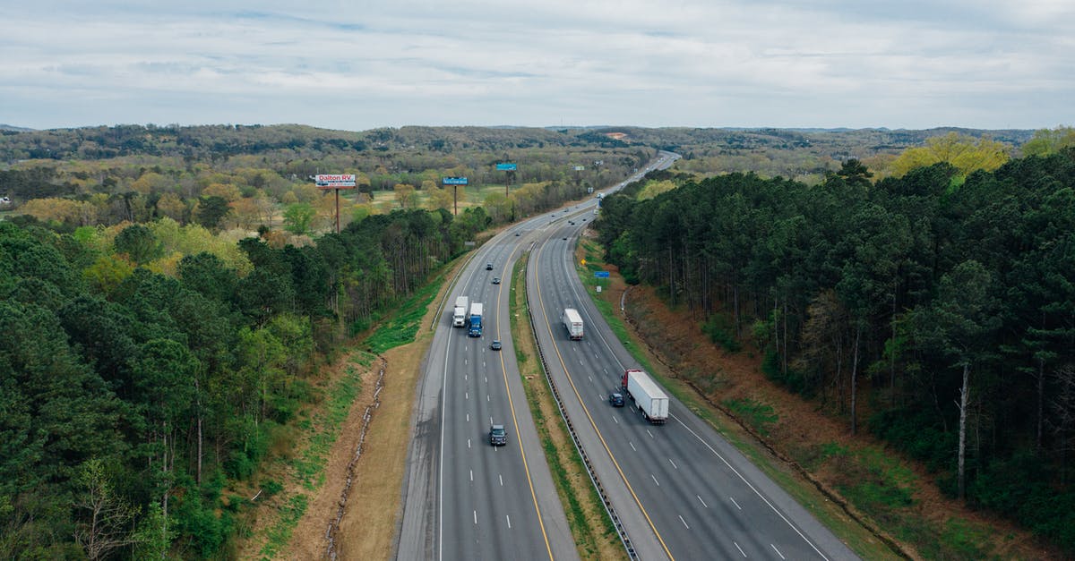 Driving in Dusseldorf´s low emission zone - Aerial view of wavy asphalt roads with driving cars and trucks between bright trees under endless cloudy sky in rural zone