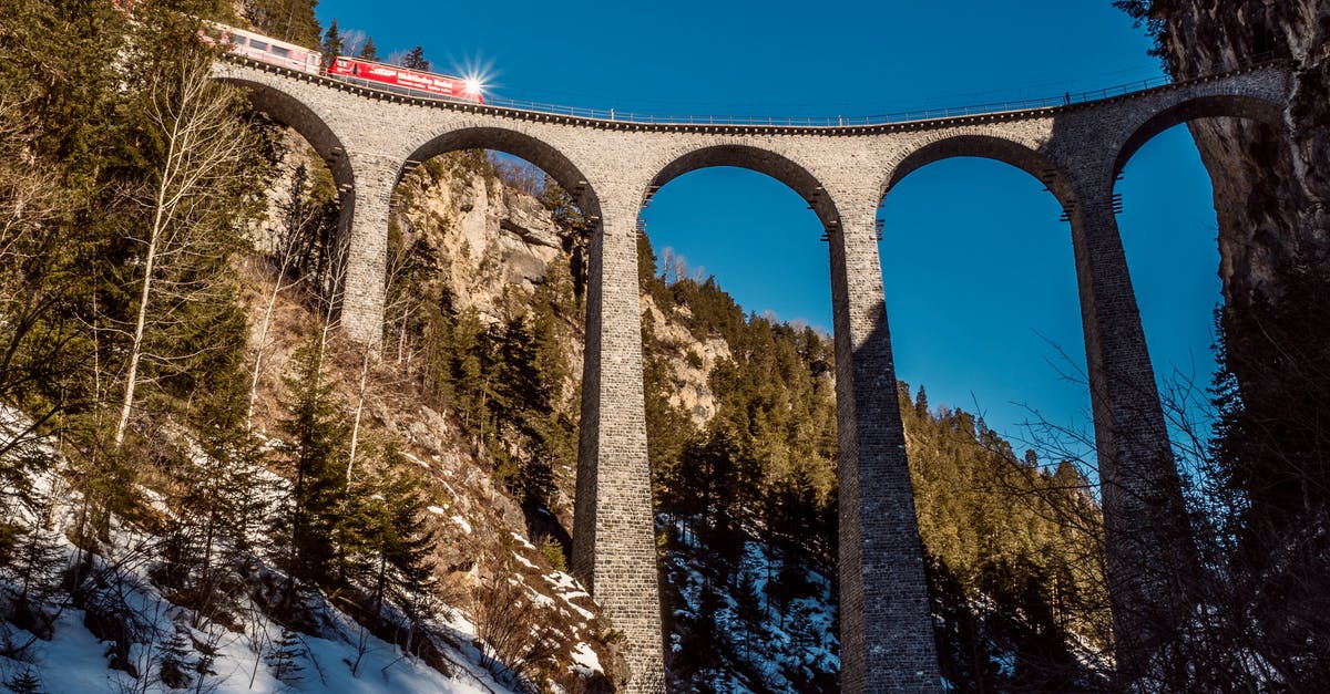 Driving in the winter (Dec-Jan) from Ohio to California - From below of train driving on arched bridge between mountains with coniferous trees under blue sky in wintertime