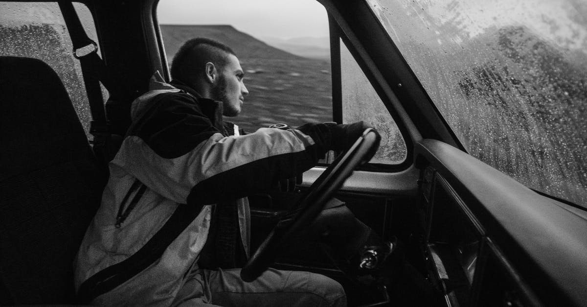 Driving non-GB registered car inside Low Emission Zone - Side view of concentrate young male traveler in warm outerwear driving car along rocky terrain during snowfall