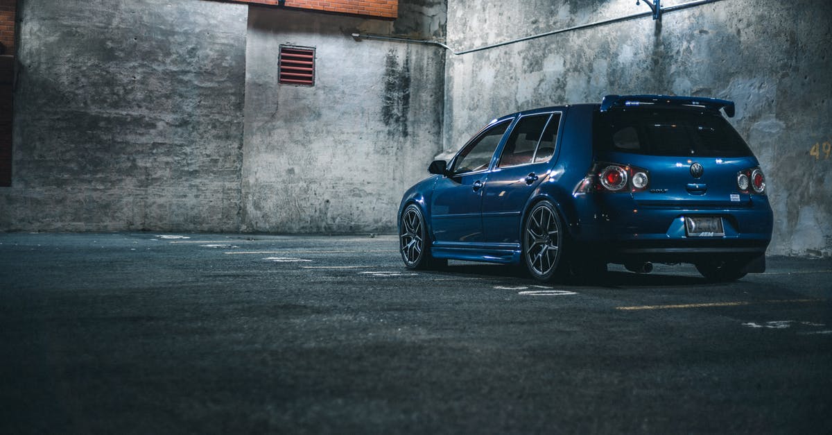 Driving Someone Else's Car Across US/Canada Borders - Blue hatchback automobile with spoiler parked on asphalt with marking lines near stone barrier in city street in evening time