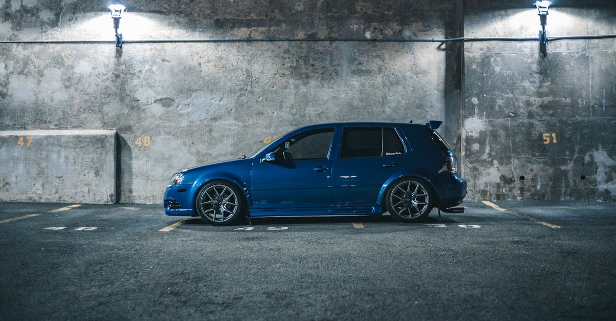 Driving Someone Else's Car Across US/Canada Borders - Side view of blue hatchback automobile placed on parking place with marking lines near cement barrier in city street in night time