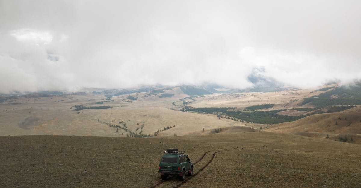 Driving SUVs in the Namibian desert - Aerial view of old green SUV car driving along empty endless valley under thick clouds