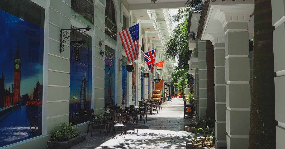 Dual citizenship (US and Ecuador) travel to China - Narrow paved street with outdoor cafe and classic styled buildings decorated with various countries flags and banners in sunlight