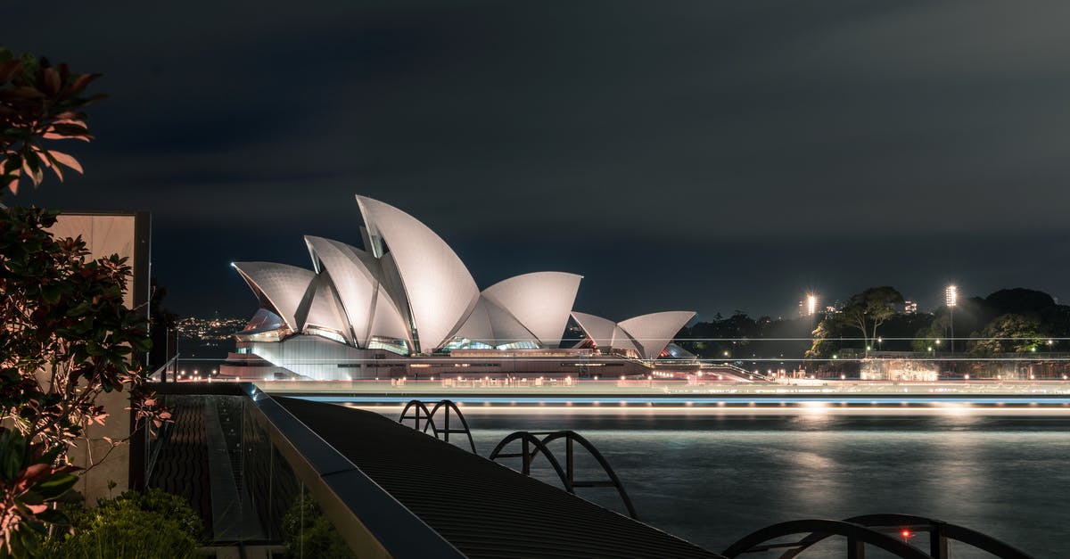 Dual national UK and Australia - Unusual design of white Sydney Opera House with large concrete panels forming shells located on city harbor at night