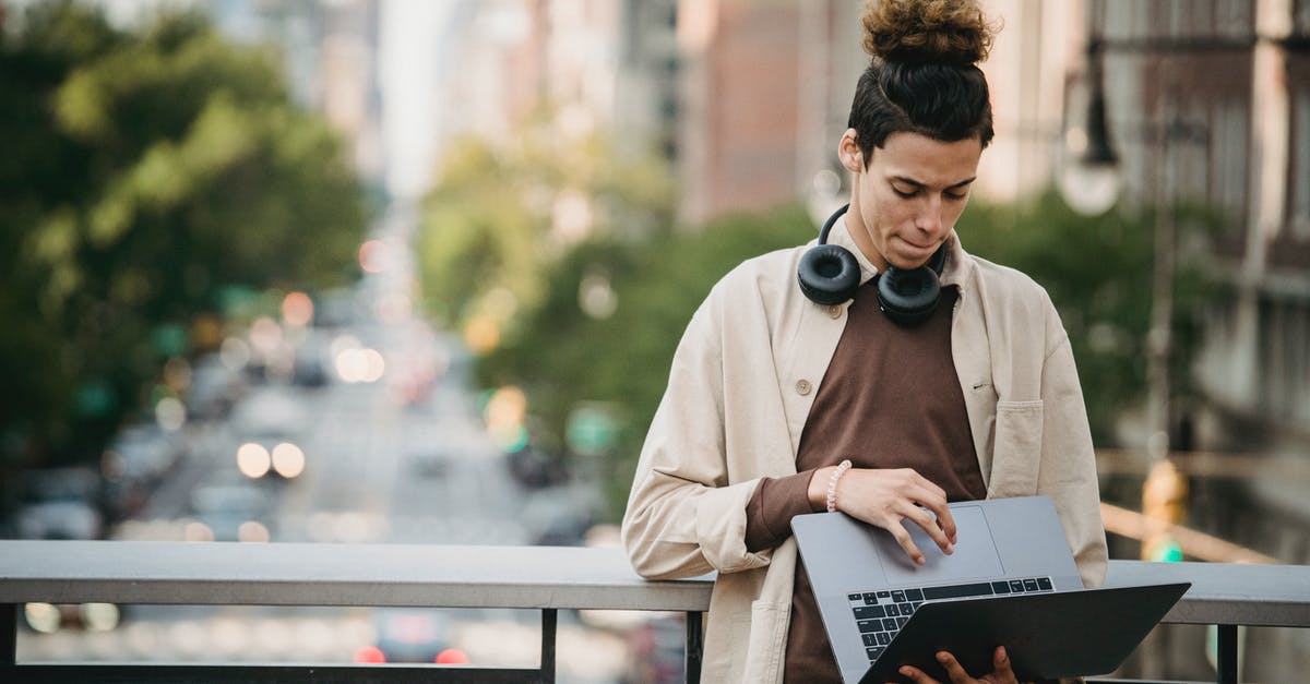 Dubai Transit (DXB) - Do you need to install DXB Smart App? - Pensive ethnic young male with trendy hairstyle downloading netbook while using touchpad on bridge on blurred background of road